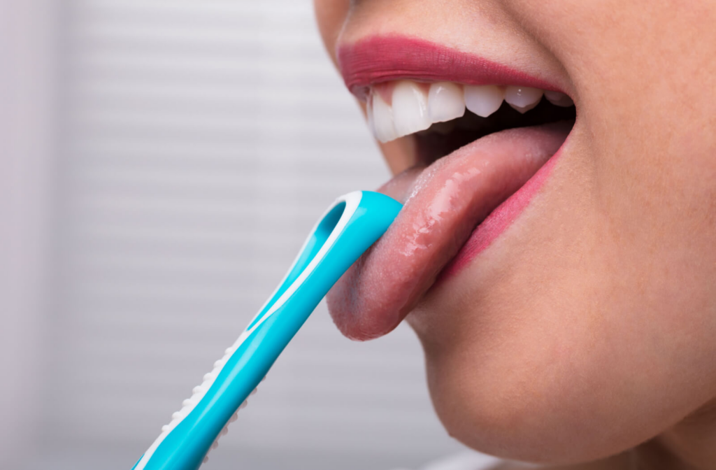 A side view close-up of a young woman cleaning her tongue using a tongue scraper.