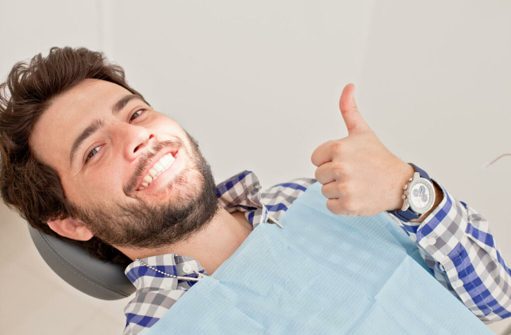 A close-up of a man smiling with a dental bib, giving a thumbs up and looking directly at the camera