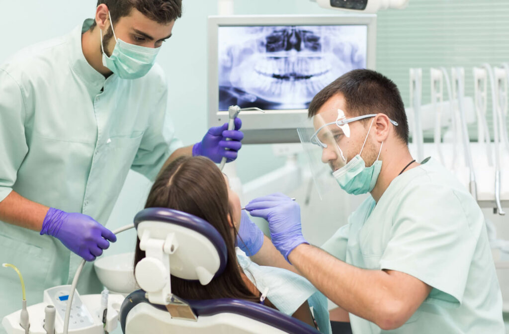 A male dentist is doing a gum grafting on a female patient in a dental chair with the help of a dentist's assistant.