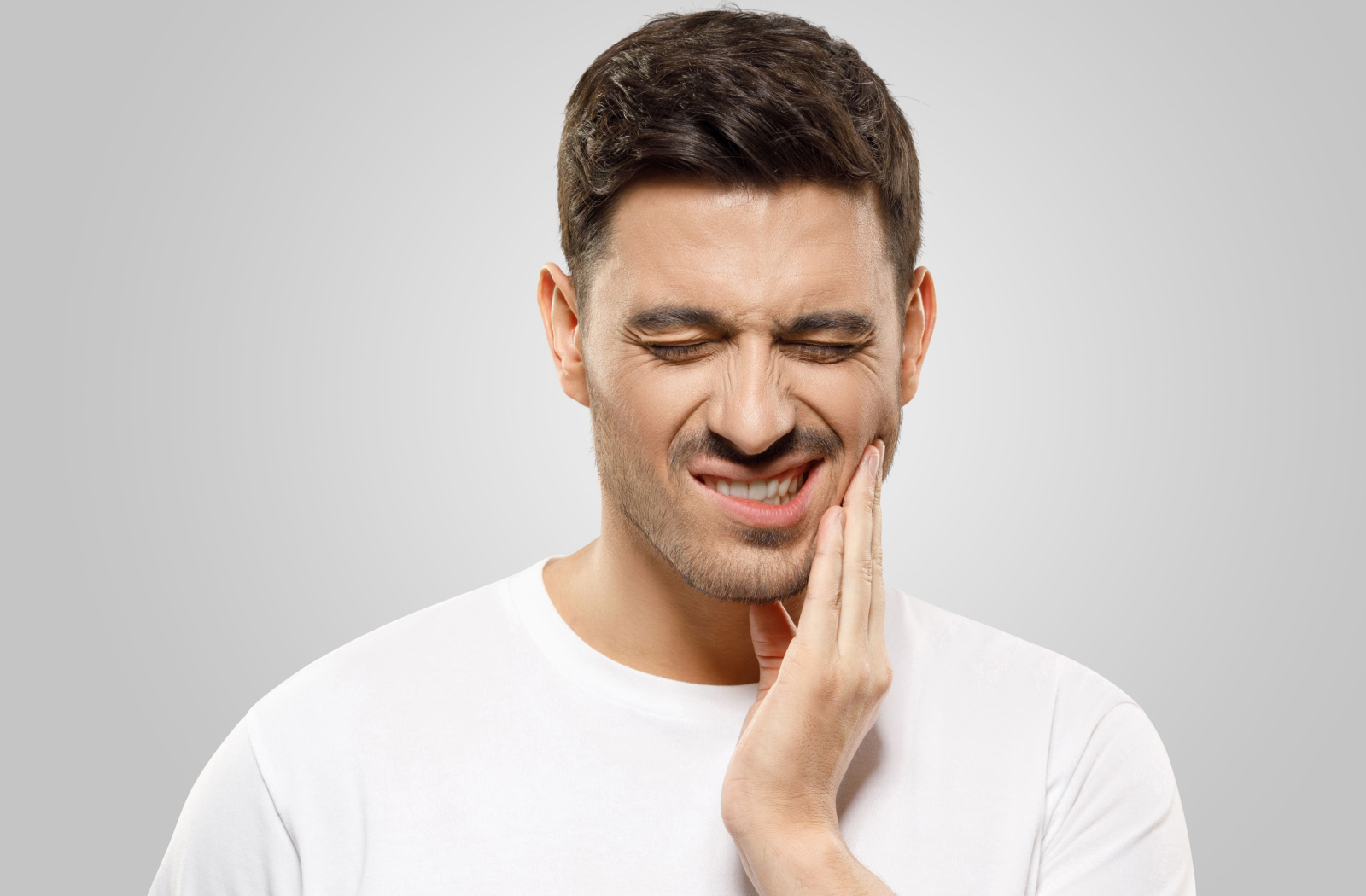 A man suffering from a toothache holds his left cheek with his left hand.
