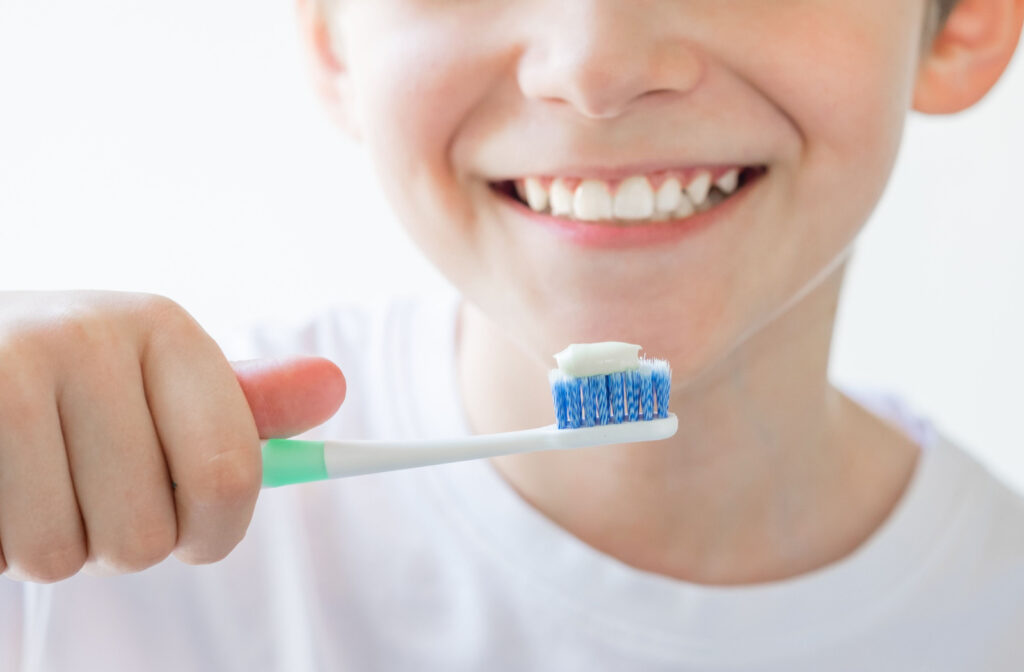 Close-up of a young childing smiling and holding a toothbrush with toothpaste on it.