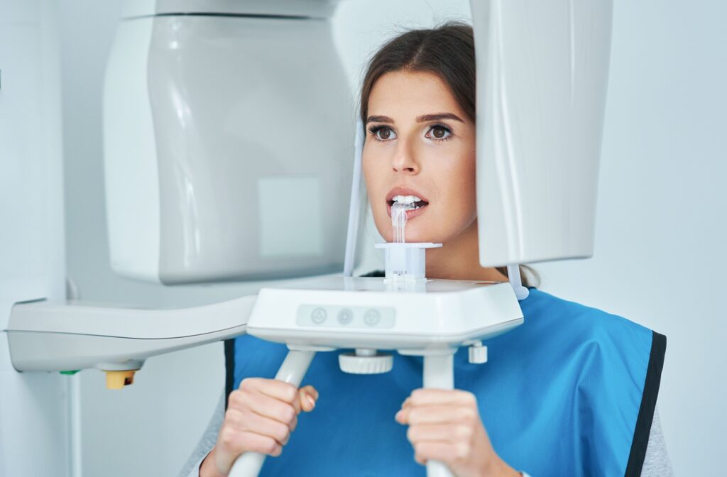 A patient stands with their face in an x-ray machine. They are wearing a blue lead apron to protect from radiation.