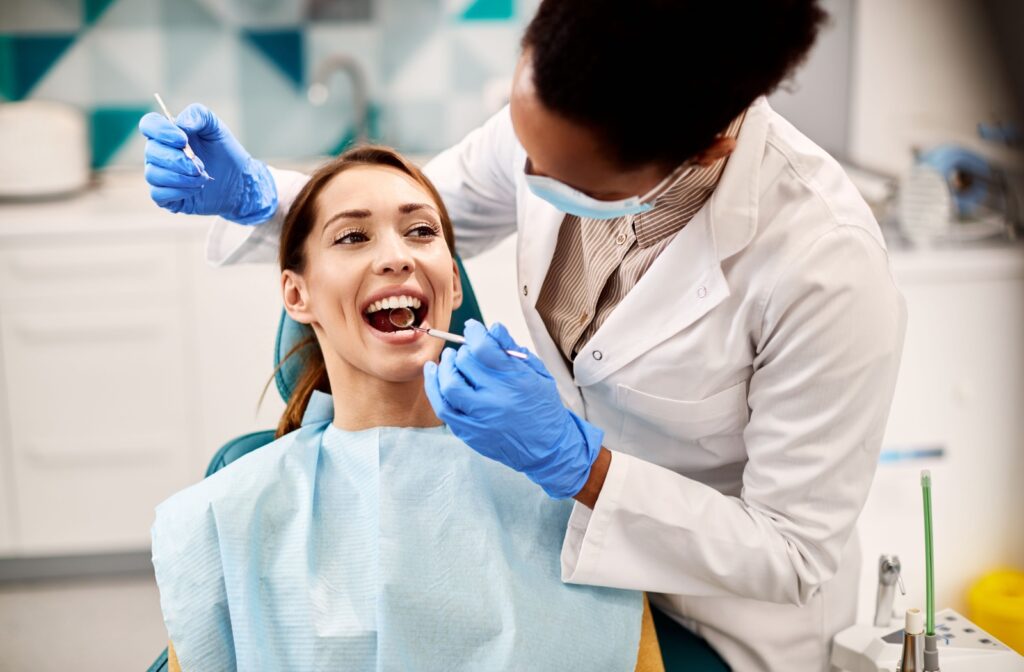 A dentist using a small mirror to examine a patients teeth at the start of a dental exam.