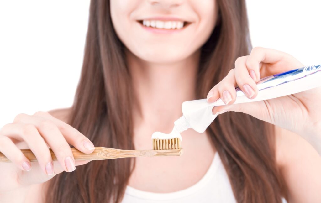 A person with veneers smiles as they squeeze toothpaste onto a bamboo toothbrush as they get ready for the day ahead.
