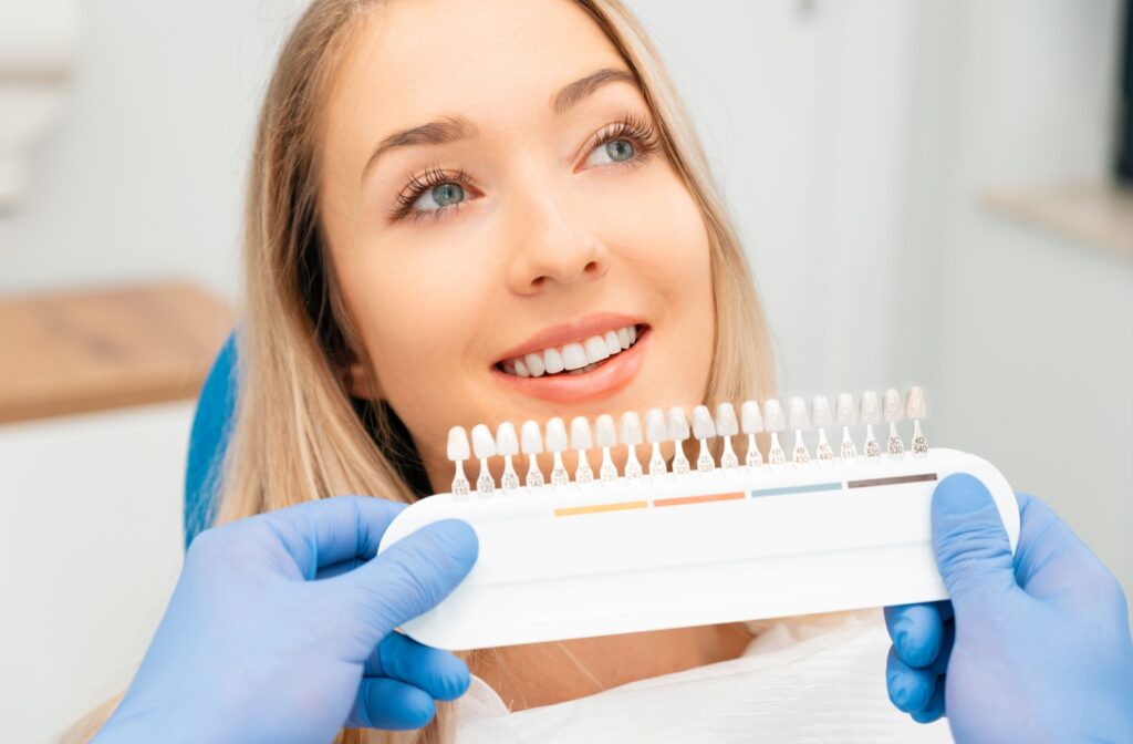 A person smiles while a dentist holds up a tooth shade guide.