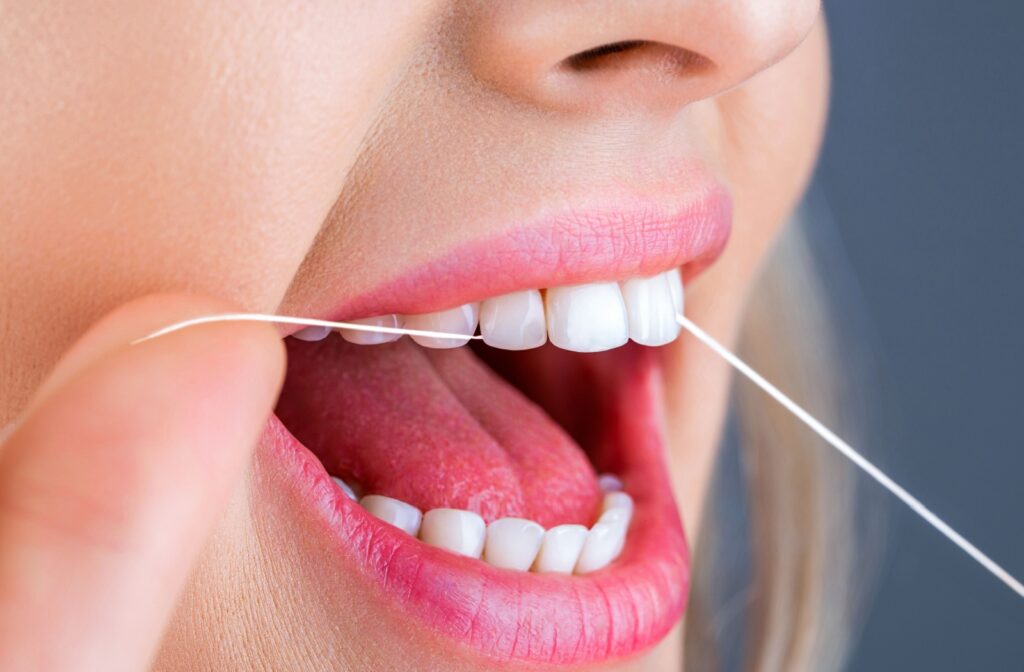 Close-up of a person flossing their teeth, focusing on the hands and dental floss between teeth.