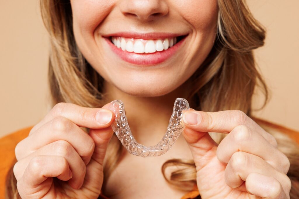 Smiling woman holding an invisalign aligner with both hands.